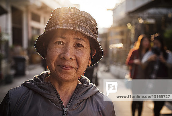 Porträt einer älteren Frau mit Eimerhut  die lächelnd in die Kamera schaut