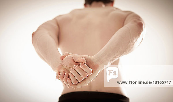 Rückenansicht eines halbnackten Mannes mit hinter dem Rücken verschränkten Händen