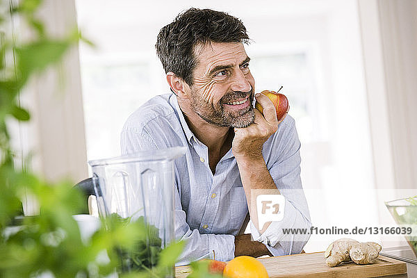 Reifer Mann isst Apfel an der Küchentheke