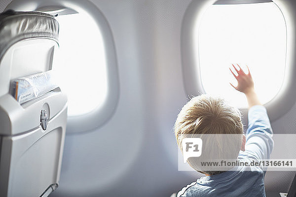 Rückansicht eines Jungen  der aus dem Flugzeugfenster winkt