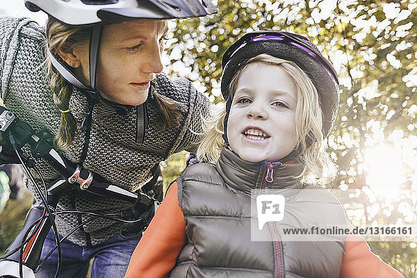 Low angle view of mother and daughter on bicycles wearing helmets looking at camera