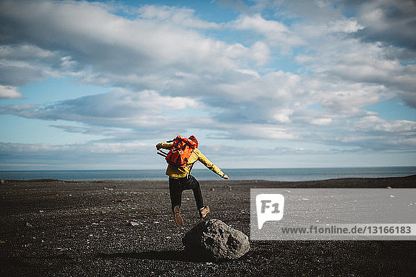 Rear view of mid adult man jumping over boulder on volcanic landscape  Iceland