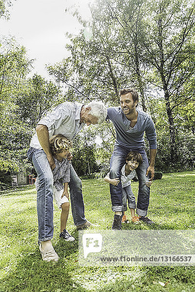 Mittelgroßer erwachsener Mann mit Vater der mit den Söhnen im Garten spielt
