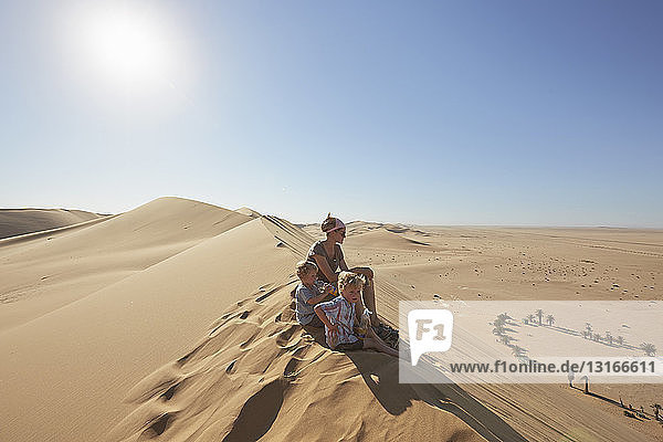 Mutter und Söhne sitzen auf einer Sanddüne  Düne 7  Namib-Naukluft-Nationalpark  Afrika