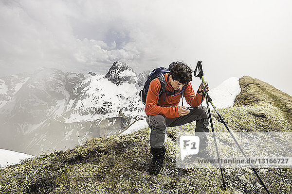 Young male mountain trekker texting on smartphone in Bavarian Alps  Oberstdorf  Bavaria  Germany