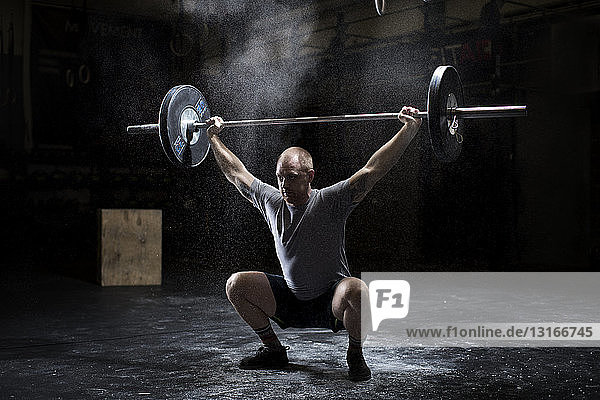 Junger Mann beim Gewichtheben von Langhantel in dunkler Turnhalle