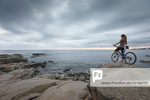 Frau steht mit Fahrrad auf Felsbrocken