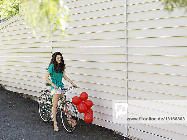 Portrait of young woman with bicycle and a bunch of balloons
