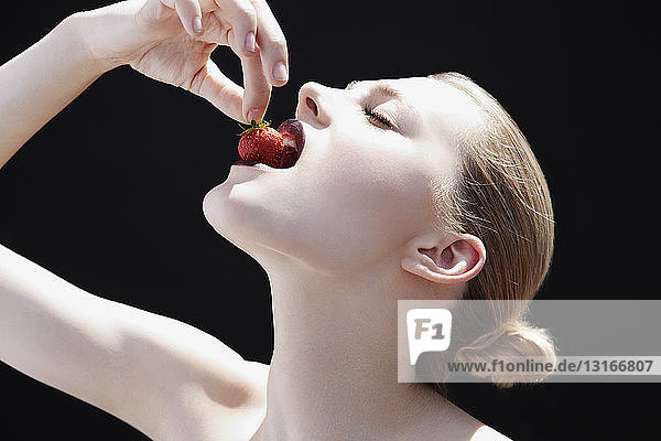 Studioaufnahme einer jungen Frau  die eine Erdbeere in den Mund nimmt