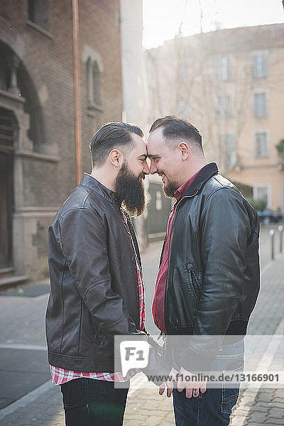Gay couple holding hands and rubbing noses on street