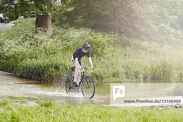 Cyclist riding over flooded road  Cotswolds  UK