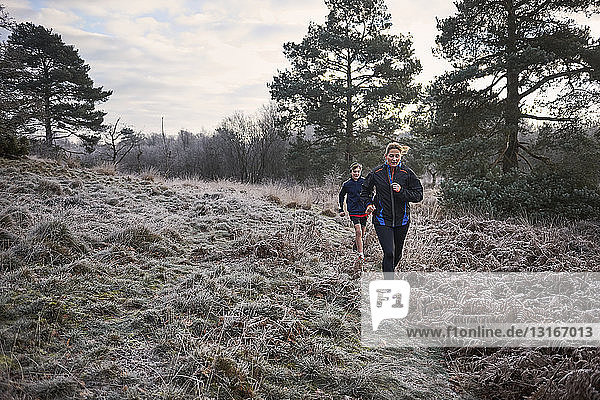 Front view of mother and son running on frosty grassland