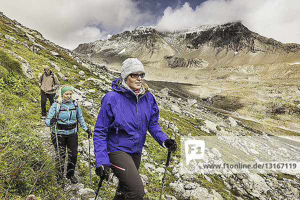 Three hikers hiking along path  Fil de Cassons  Segnesboden  Graubunden  Switzerland