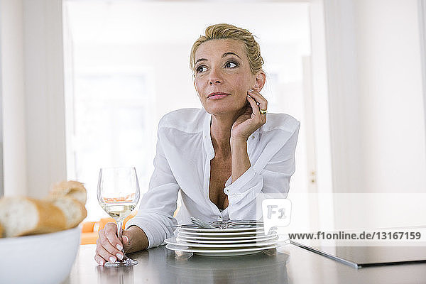 Mature woman daydreaming whilst drinking wine at kitchen counter