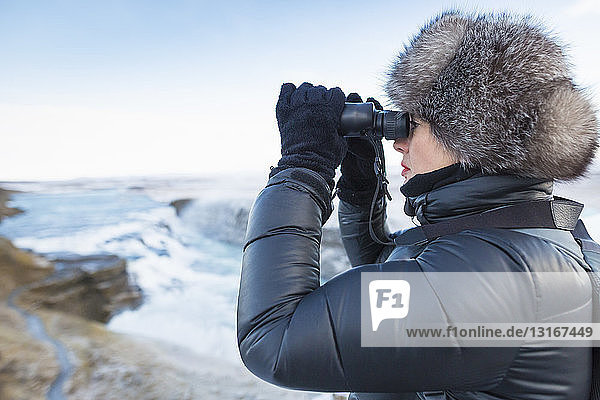 Woman using binoculars to look at Gullfoss Waterfall  located in the canyon of Hvita River in South West Iceland