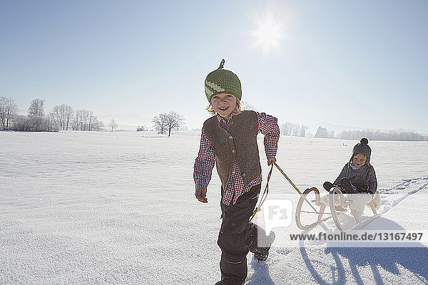 Young boy pulling brother on sled