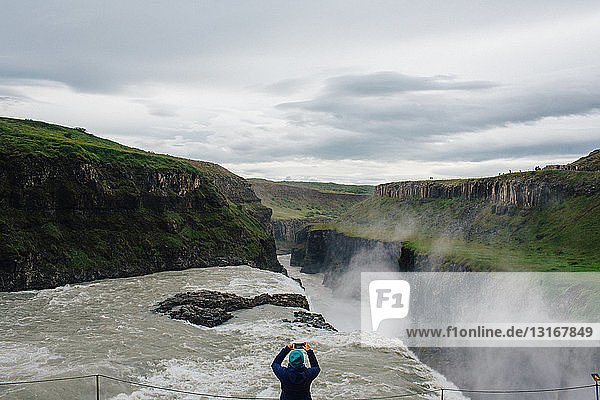 High angle rear view of mid adult woman using smartphone to photograph waterfall  Iceland