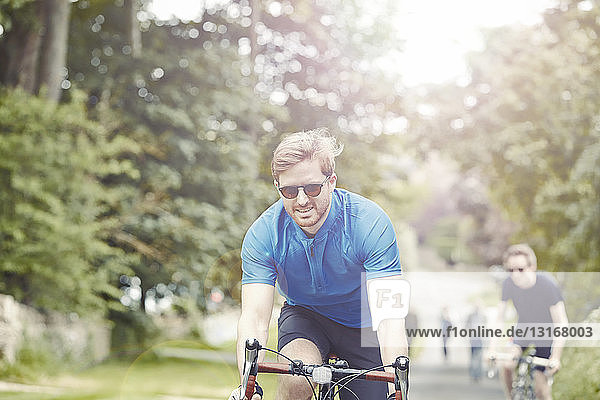 Cyclists riding on leafy countryside road Cotswolds UK