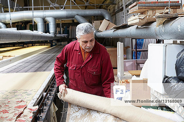 Mann hält Stoffrolle in Textilfabrik