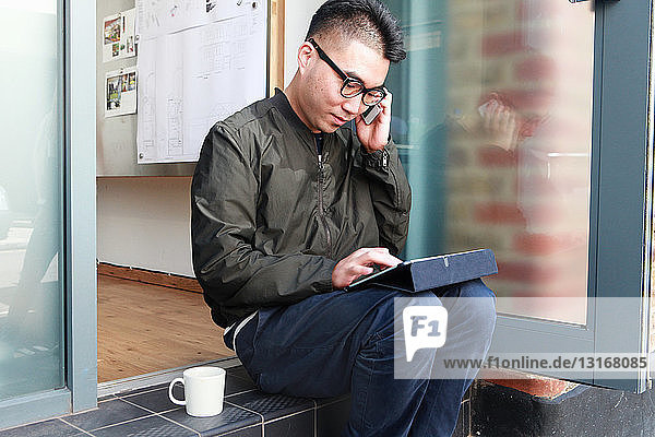 Männlicher Architekt benutzt Smartphone und digitales Tablet auf Bürostufe