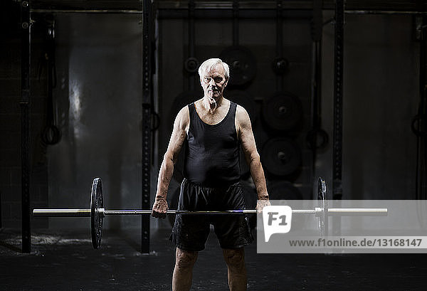 Seniormann beim Gewichtheben von Langhantel in dunkler Turnhalle