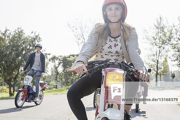 Group of friends riding mopeds along road  young female rider in foreground