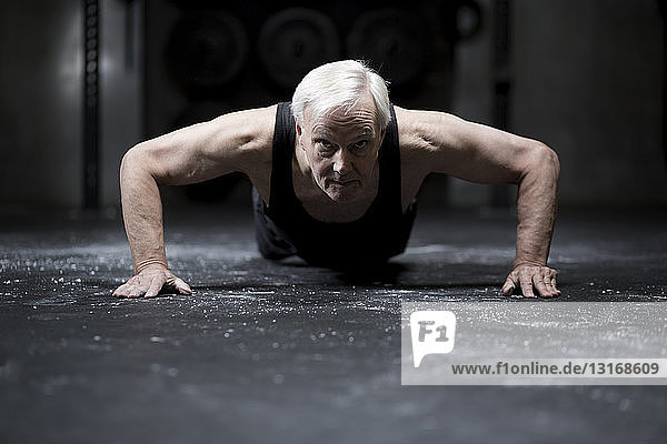 Surface level view of senior man doing push ups in dark gym