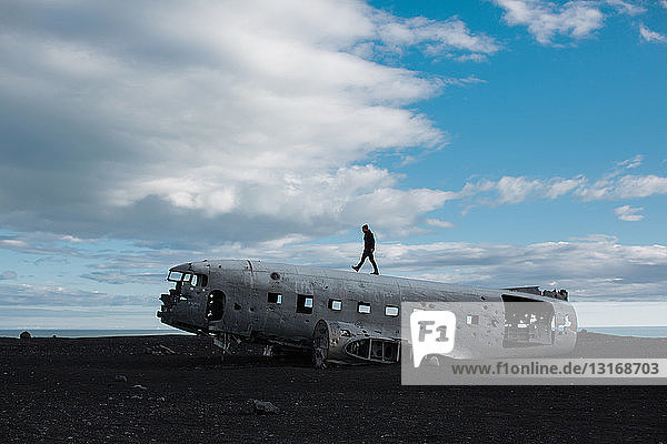 Seitenansicht eines mittelgroßen Mannes  der auf einem Flugzeugwrack in vulkanischer Landschaft geht  Island