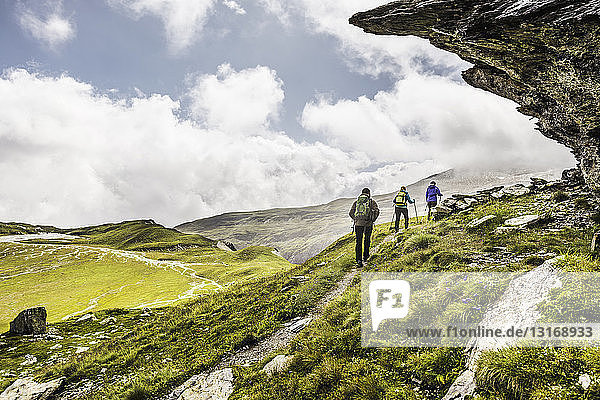 Rückansicht von drei Wanderern  die unter einem Felsüberhang wandern  Fil de Cassons  Segnesboden  Graubünden  Schweiz