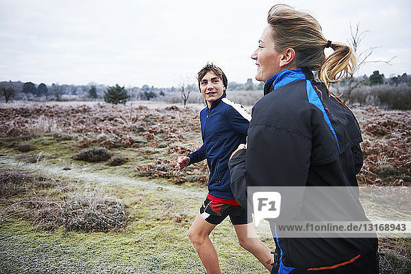 Side view of mother and son running on frosty grassland smiling
