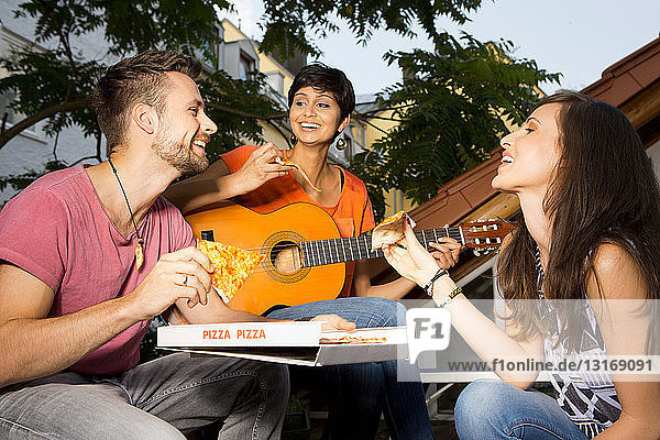 Three friends eating pizza woman playing guitar