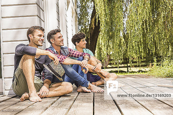 Drei Männer sitzen auf einer Holzterrasse und schauen weg