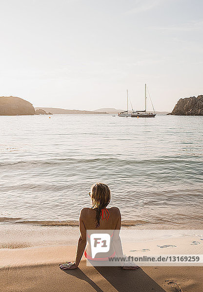 Rear view of woman sitting looking out from beach  Menorca  Balearic islands  Spain