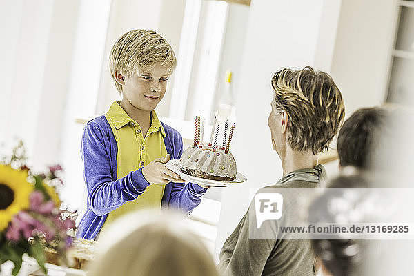 Boy handing grandmother birthday cake at party in dining room