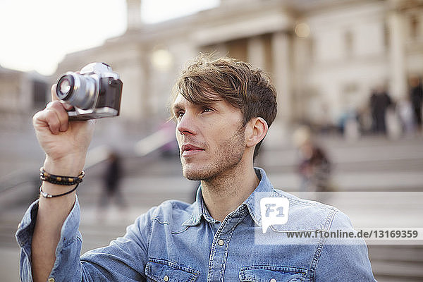 Mid adult man taking photographs at Trafalgar Square fountain  London  UK