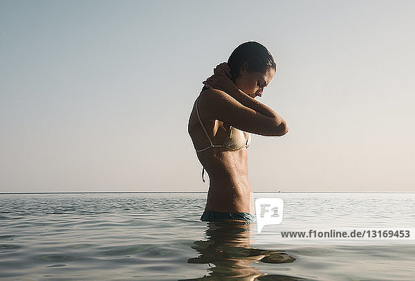 Beautiful young woman with hands behind neck in sea