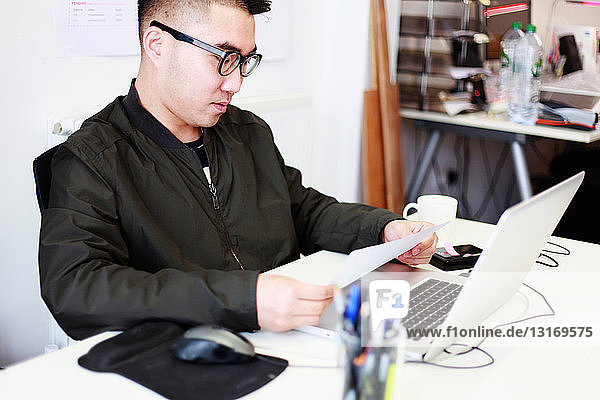 Male architect reading paperwork at office desk
