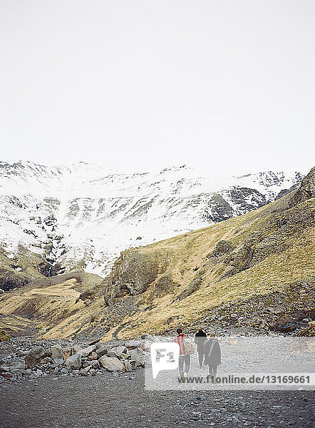 Rückansicht von drei Touristen  die auf schneebedeckte Berge zulaufen  Island