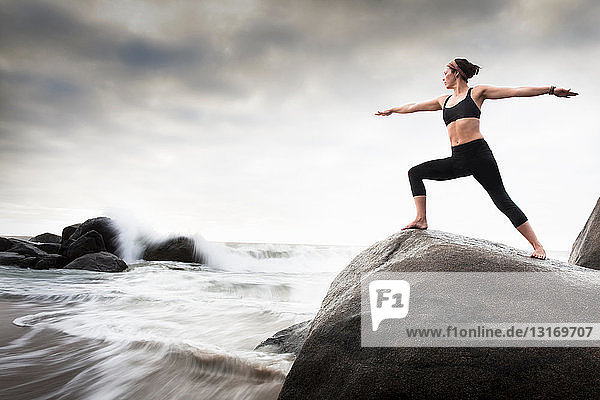Frau praktiziert Yoga auf Felsen am Strand