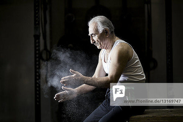 Älterer Mann sitzt kreidebleich an den Händen in dunkler Turnhalle