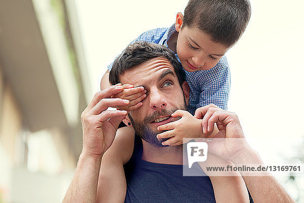 Vater trägt Sohn auf den Schultern  Junge bedeckt das Auge des Mannes