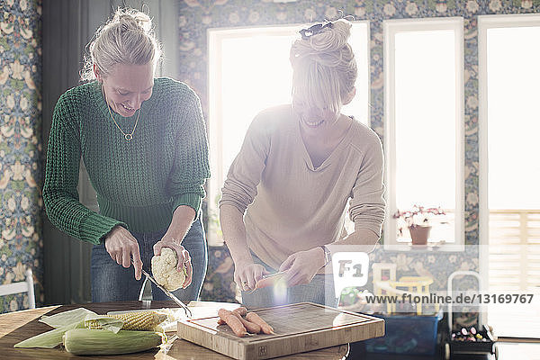 Two female friends preparing organic vegetables in kitchen