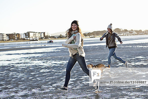 Two female friends running with dog on the beach