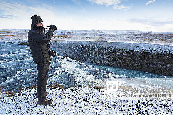 Älterer Mann fotografiert den Gullfoss-Wasserfall in der Schlucht des Hvita-Flusses in Südwest-Island