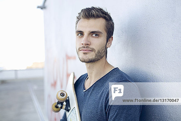Porträt eines jungen Mannes der ein Skateboard hält und wegschaut