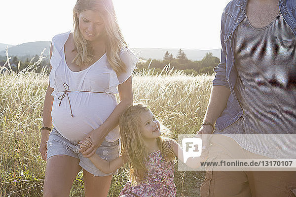 Pregnant couple and daughter strolling in field