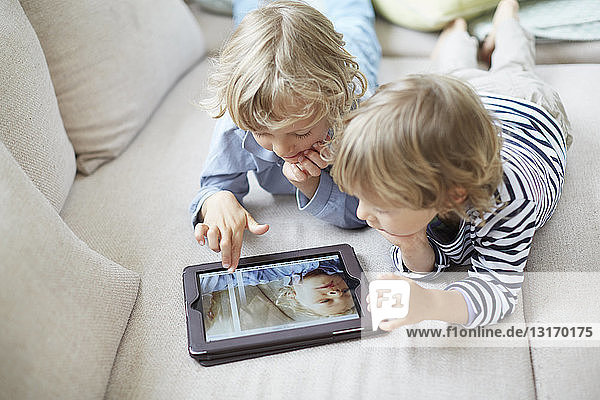 Zwei Jungen liegen vorne nebeneinander auf dem Sofa und benutzen ein digitales Tablett