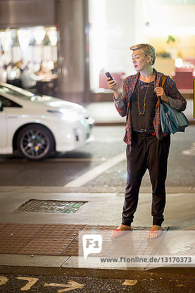 Mature woman texting on smartphone in the street at night  London  UK