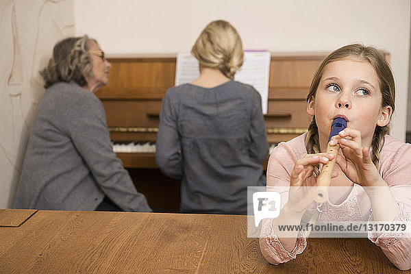 Mädchen spielt Blockflöte  während die Schwester am Klavier von der Großmutter beobachtet wird