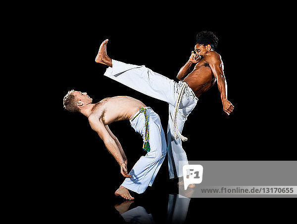 Zwei Männer üben Capoeira  der eine tritt aus und der andere beugt sich nach hinten